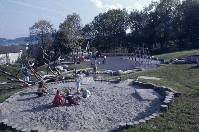 "Siedlungs- und Quartierspielplätze: Siedlungsspielplatz Adliswil ZH" - Blick auf den Spielplatz, Kinder spielen im Sandkasten, auf dem Kletterbaum, auf dem Hartplatz; um 1970