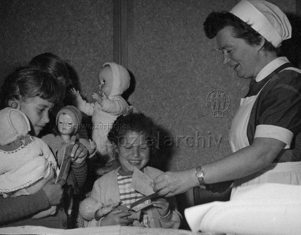 Frau überreicht zwei Mädchen Puppen als Geschenk; um 1965