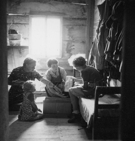 Praktikantinnenhilfe - Mutter, Praktikantin und zwei Kinder beim Verpacken von Wäsche; um 1965