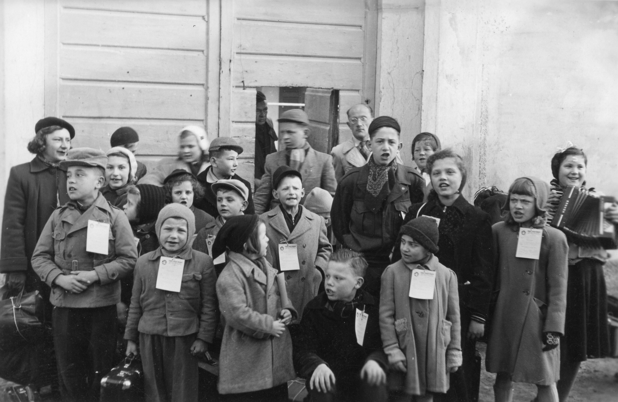 Tschechische Kinder in Brusata, Dezember 1951 bis März 1952; eine Gruppe von Flüchtlingskindern sowie deren Betreuer possieren singend und musizierend vor einem Gebäudeeingang