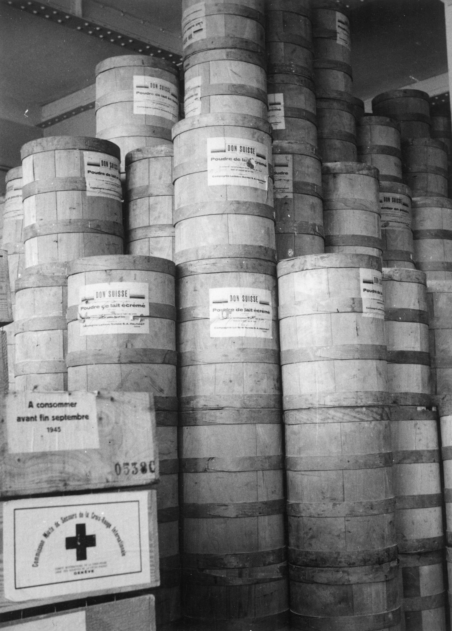 "Lyon 1945. Leere Milch(pulver)fässer im Lager." Beschriftung: "Don Suisse. Poudre de lait écrémé. [...] Compagnie Laitière Suisse S.A. Hochdorf (Suisse)." Kiste: "A consommer avant fin septembre 1945."
