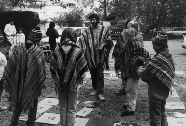 "Spielaktion Versoix 1990" - Kinder und ein Leiter mit Ponchos beim Spielen