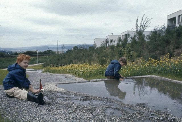 "Betoniertes Bächlein, Urdorf" - zwei Jungen beim Spielen mit kleinem Segelschiff; um 1990