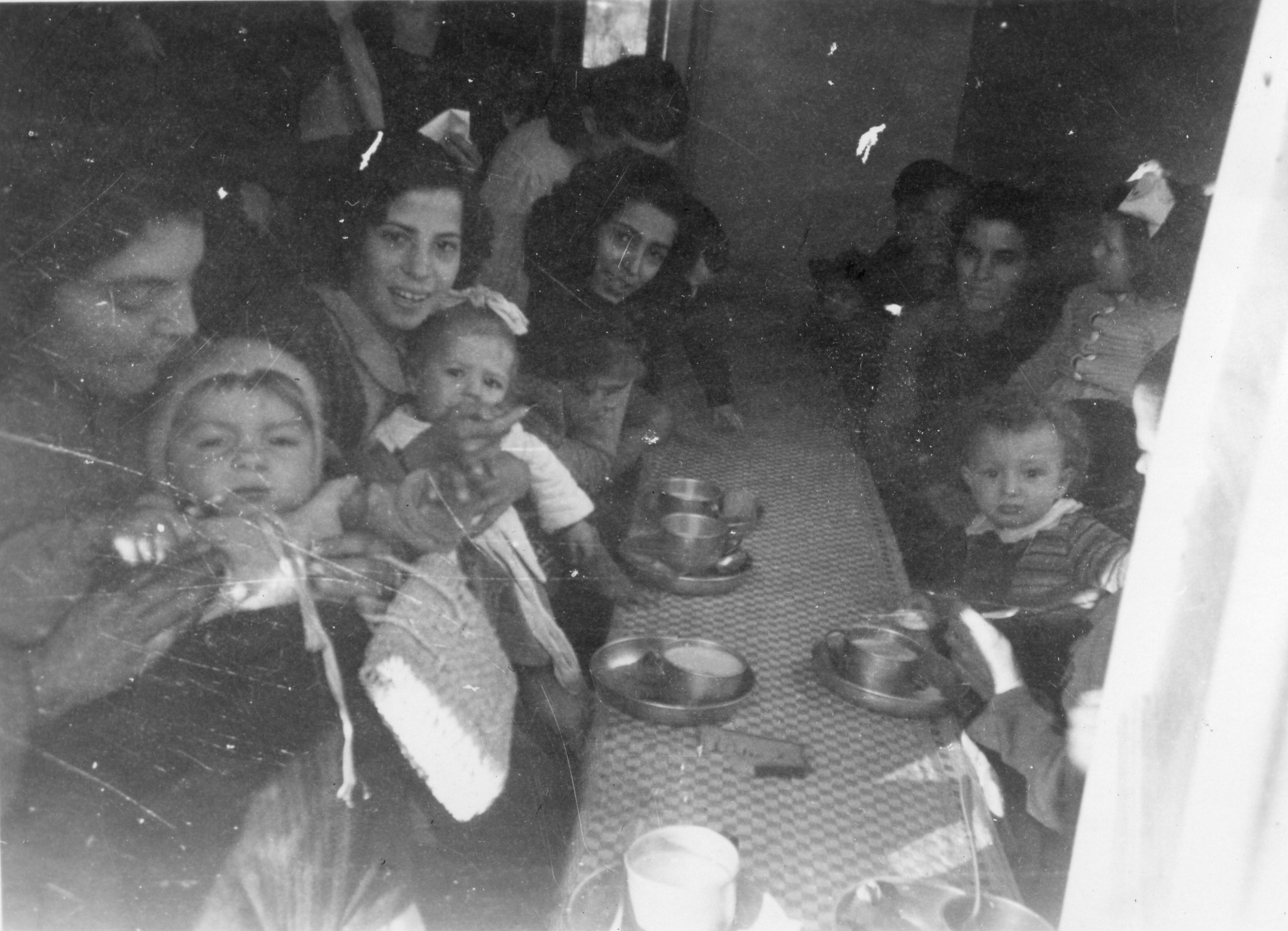 "Venaria Okt. 1946. Die Merenda (Zvieri) ist im vollem Gang."; Frauen und Kinder sitzen an einem Tisch und essen eine Zwischenmahlzeit