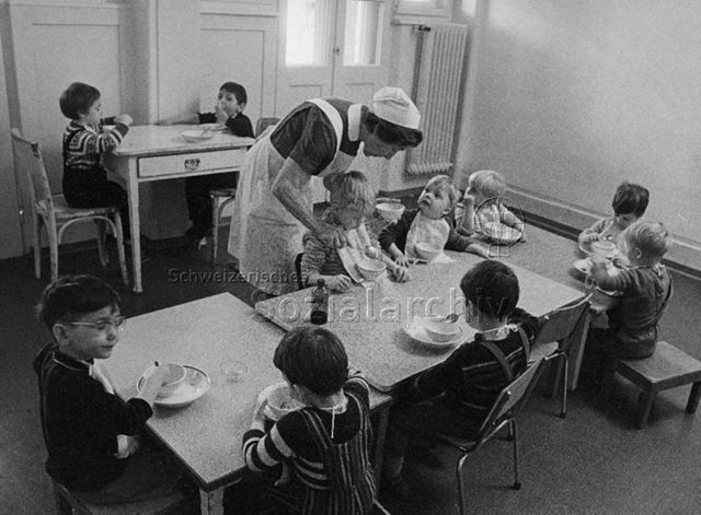 "Kinderheilstätte [Davos], Essen" - Kinder am Tisch, Krankenschwester beim Schöpfen von Essen; 1971