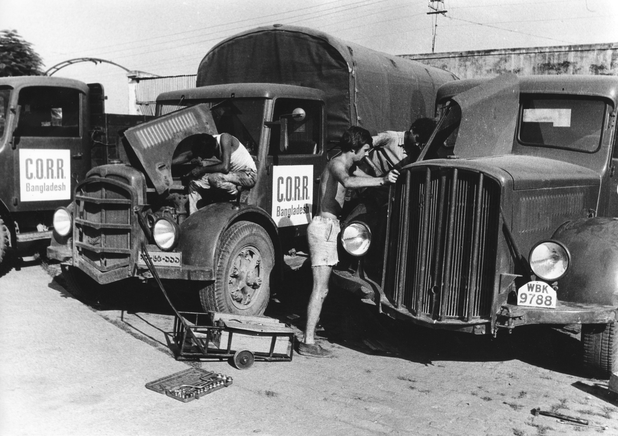 "Bangladesh: Swiss Truck Team Oktober 1972"; ein Schweizer Fachmann wartet mit Einheimischen mehrere Hilfsgüterlastwagen