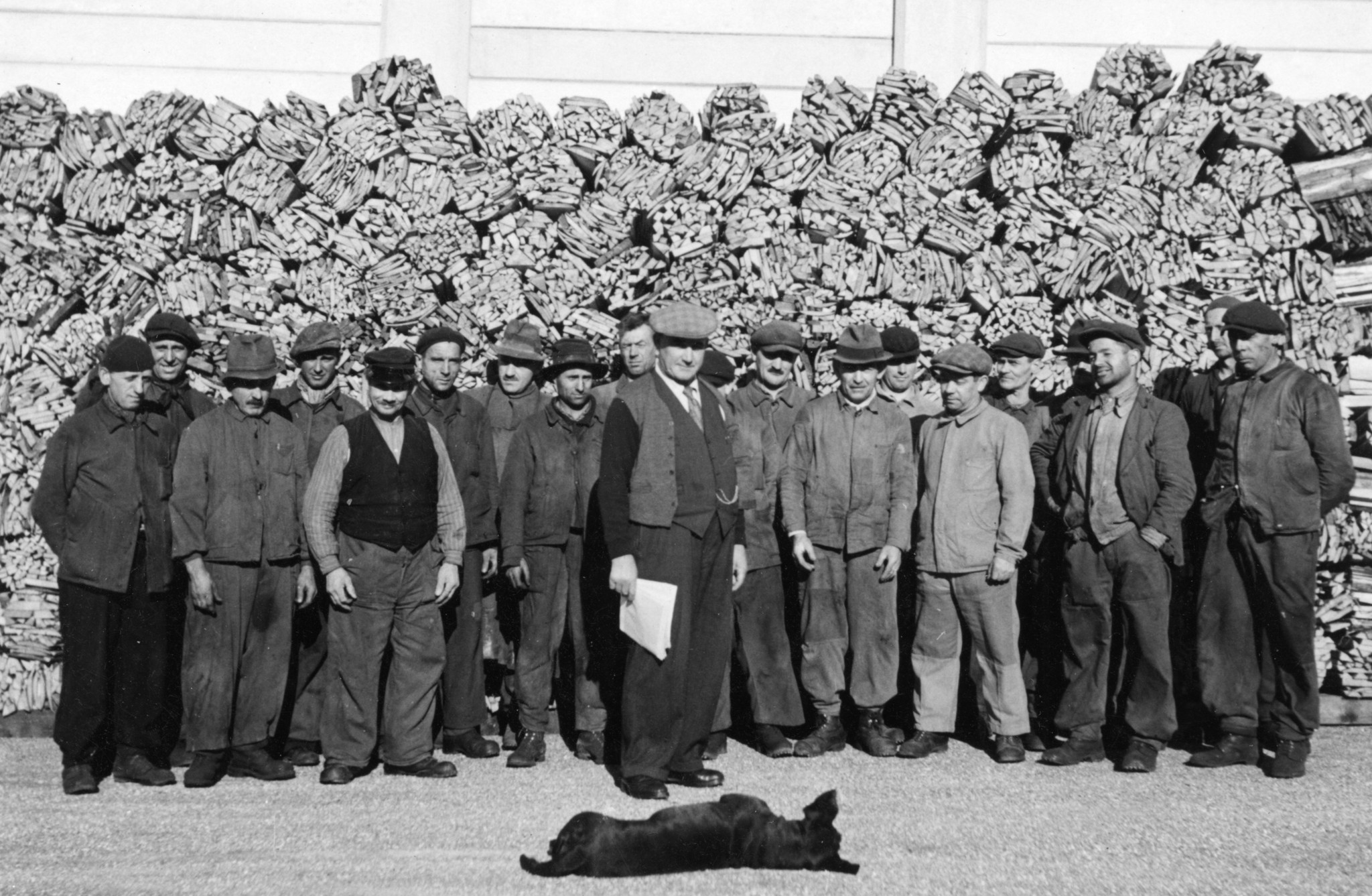 Gruppenbild mit Männern und einem Hund vor einem Haufen Brennholz