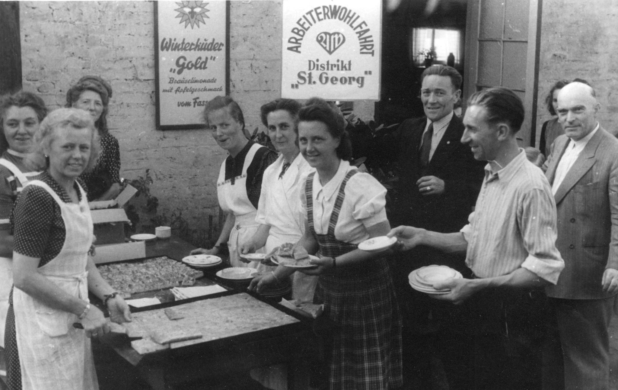 "Vorstand der AWO (Arbeiterwohlfahrt"; Frauen und Männer stehen um einen Tisch und essen Kuchen