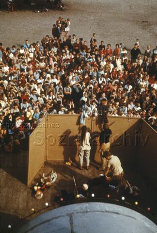 "Kasperli, Handpuppen: Kasperlispiel" - Blick von hinter der Bühne, Schauspieler halten Puppen über eine Stellwand, dahinter sitzen und stehen zahlreiche Kinder und verfolgen die Vorstellung; um 1970