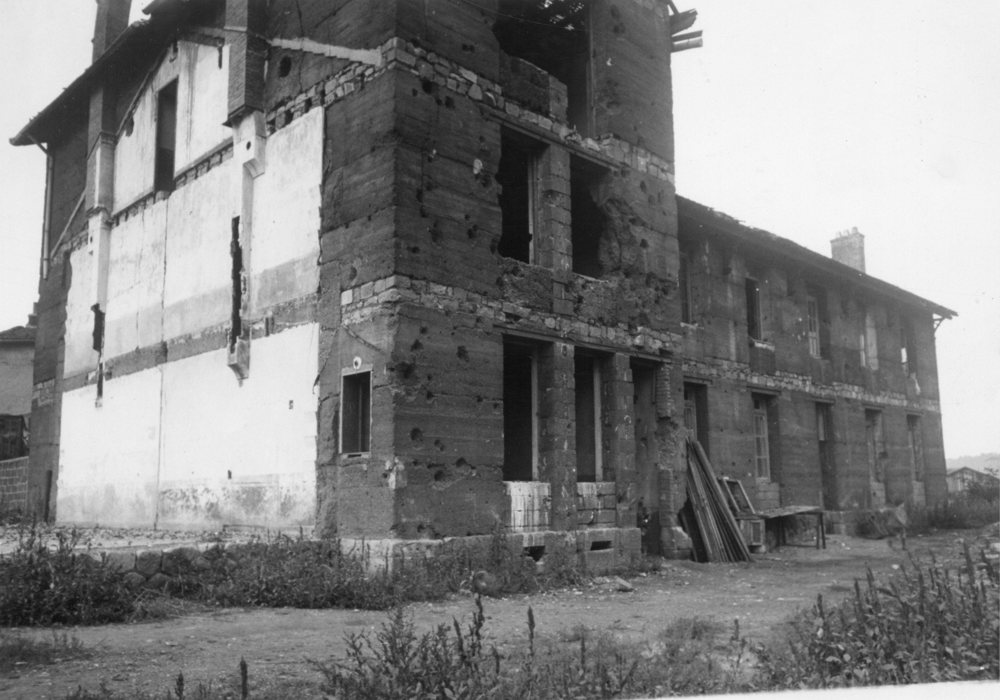 "Saint-Etienne, 1945. Wohnhaus der Bergarbeiterfamilie Grenados. Im Vordergrund, anschliessend an das Haus, sieht man den Grundstein und Feuermauer des zerstörten Hauses, ursprüngliche Wohnung der Familie."