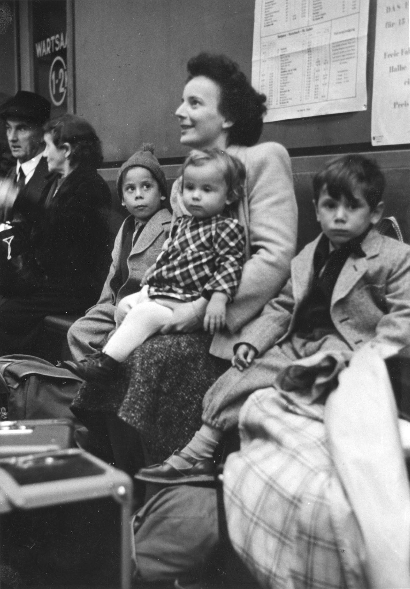 "Austral. flücht. ...?" Eine Frau und drei Kleinkinder auf einer Bank sitzend, vermutlich in einer Wartehalle eines Bahnhofes