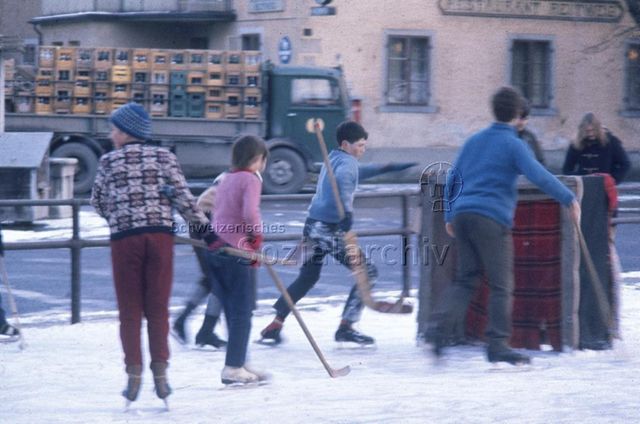 "Die gefrorene Spielwiese, Winterthur" - Kinder beim Eishockeyspielen auf dem Rindermarktplatz im Wildbachquartier, im Hintergrund Restaurant Reitweg; um 1970