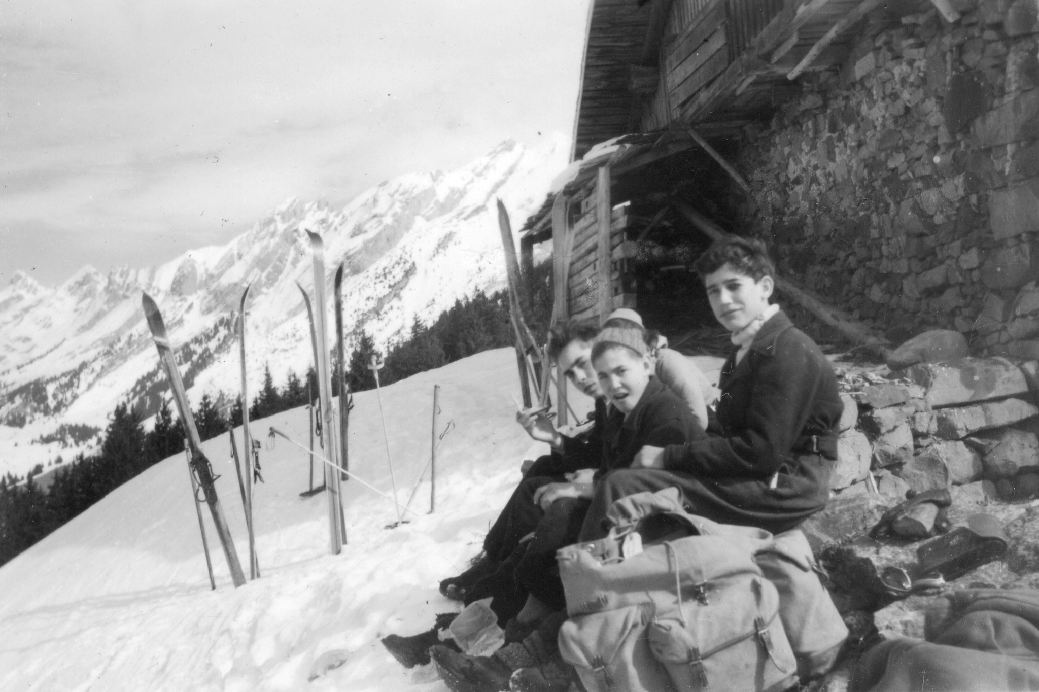 Drei Knaben sitzen auf einer Mauer im Schnee, im Vordergrund Rucksäcke, im Hintergrund Skier