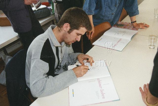 "Pressekonferenz Verlag 'Schöner lieben' vom 06.05.1996" - Mann beim Zeichnen in ein Buch