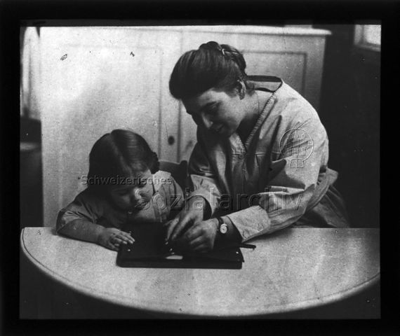 Diaserie zum Thema Kindergarten / Schulkind; ein Mädchen und eine Frau sitzen an einem Tisch; um 1930