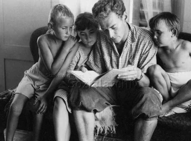 PraktikantInnenhilfe - Praktikant liest Kindern aus einem Buch vor; um 1965