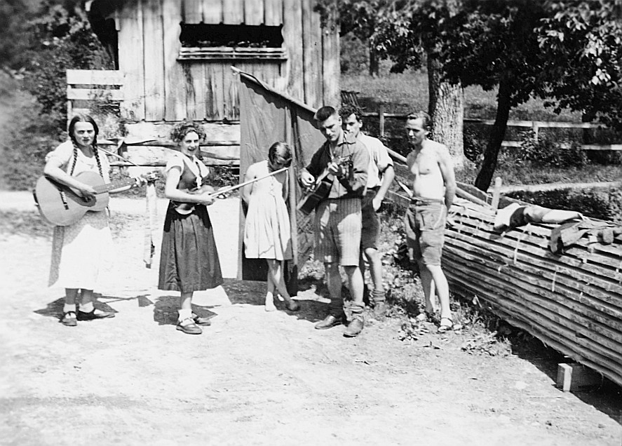 Das Hofsingen kann beginnen - Gruppenporträt Wandervögel: Zwei Wandervögel spielen Gitarre, ein Wandervogel Geige tragend (1936)