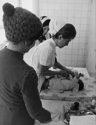 "Mütterberatung" - Krankenschwester kümmert sich um Säugling, Mutter sieht zu; 1970