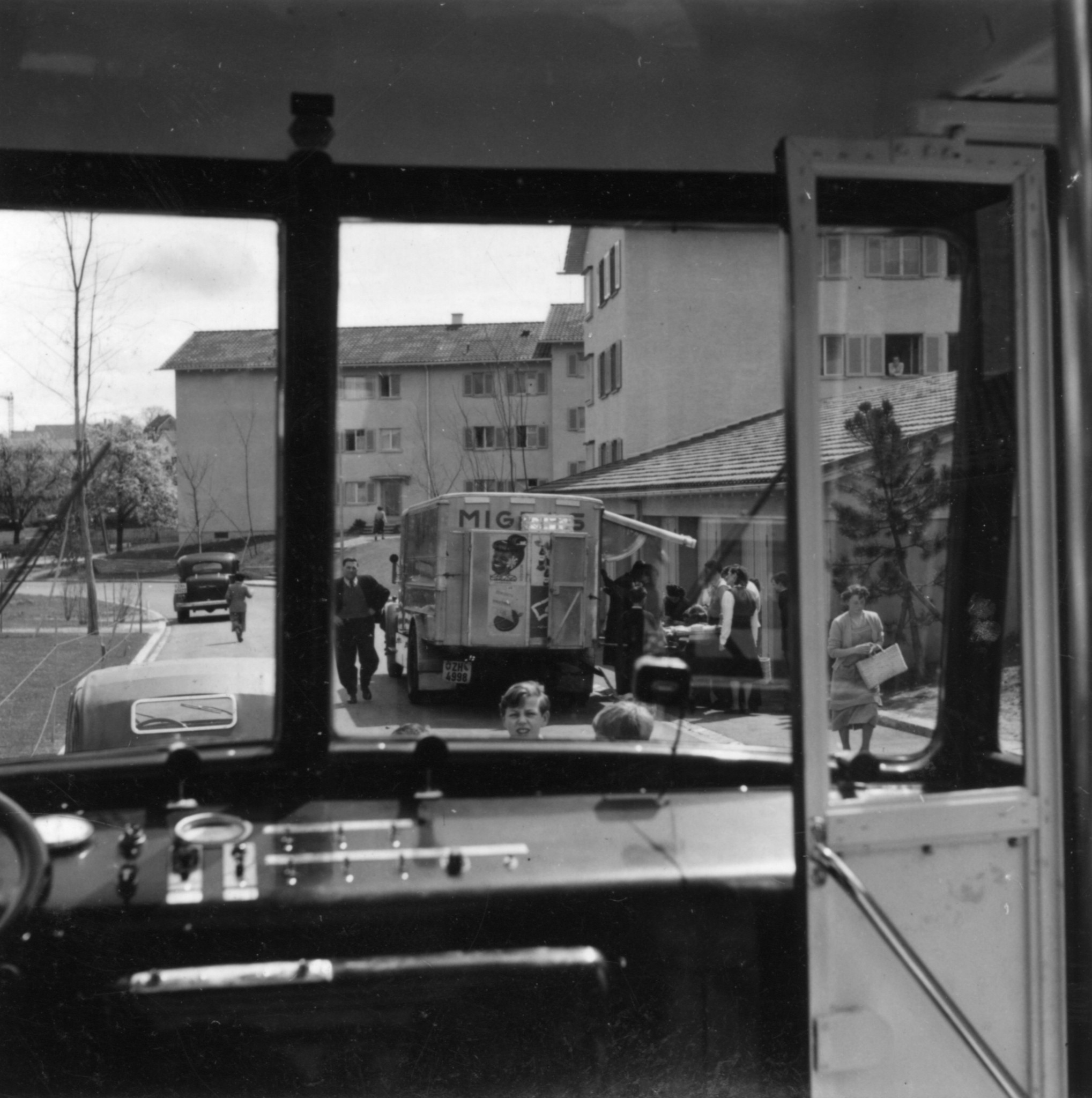 Blick aus einem Verkaufswagen des Lebensmittelvereins Zürich auf einen Verkaufswagen der Migros und Passanten