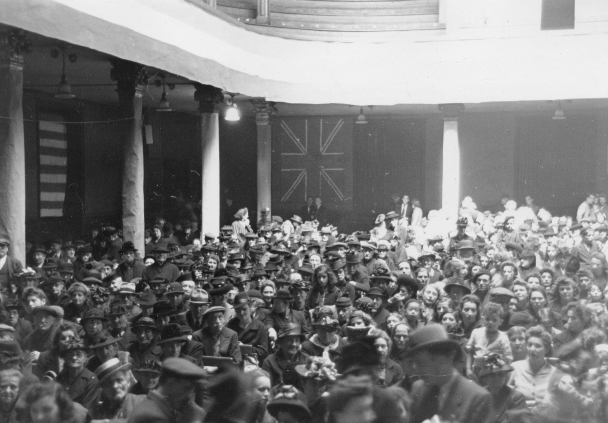"St. Etienne. 26. Mai 1945. Jahrestagfeier der Bombardierung in der Bourse du Travail. St. Etienne. 26. Mai 1945. Anniversaire du bombardement à la Bourse du Travail" ; Zahlreiche Personen feiern die Jahrestagfeier der Bombardierung im Gewerksch