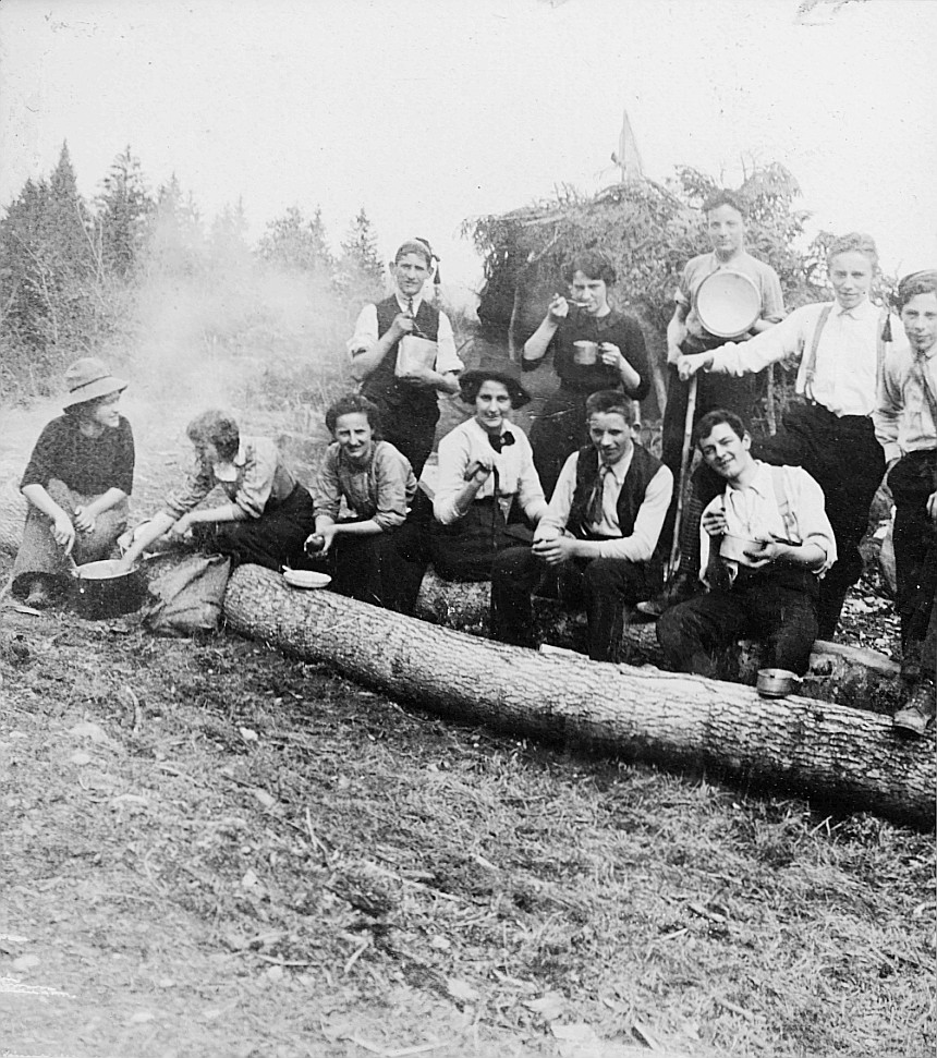 Wandervögel der Wandervogel-Ortsgruppe Zürich-Altstadt sitzen oder stehen bei einem abgeholzten Stammbaum während einer Mahlzeit (19