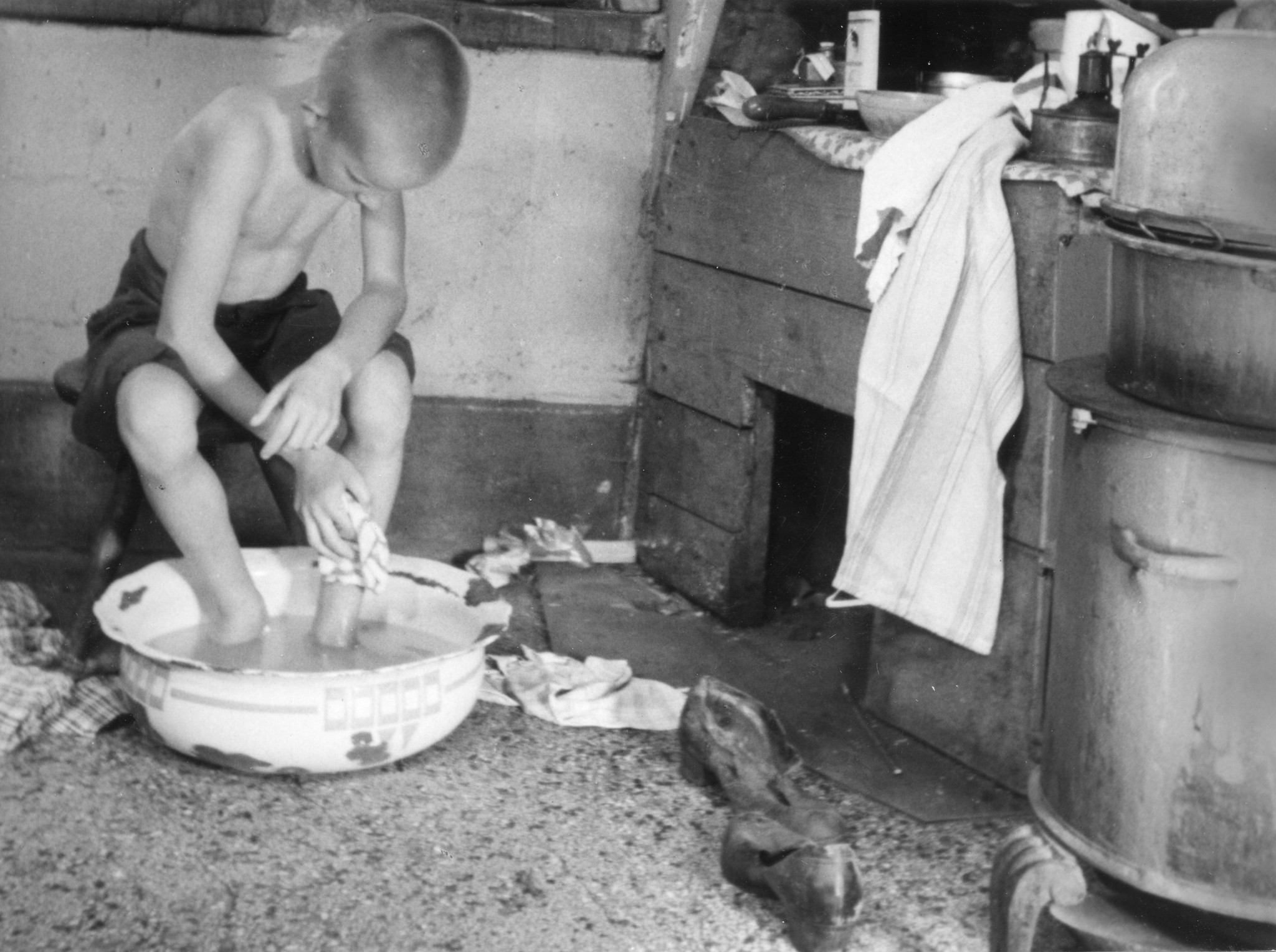 "Vor der Reis (aus ungesunden und unfreundlichen Wohnungen holen wir unsere Kinder)"; ein Knabe wäscht sich mit einer Schüssel Wasser die Beine