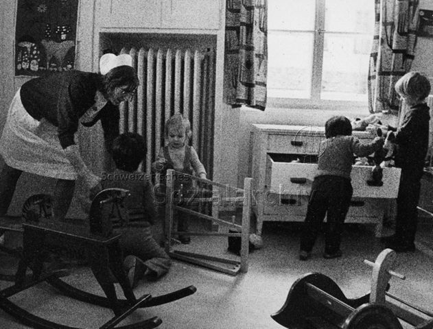 "Kinderheilstätte [Davos], Bei den Kleinen" - Betreuerin und vier Kinder beim Spielen; 1972